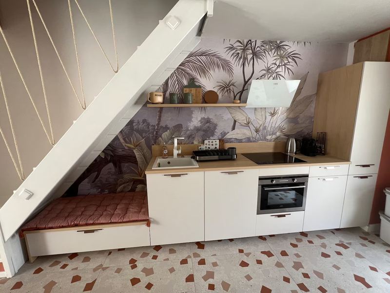 Cuisine ouverte sous l'escalier, papier peint palmiers et banquette